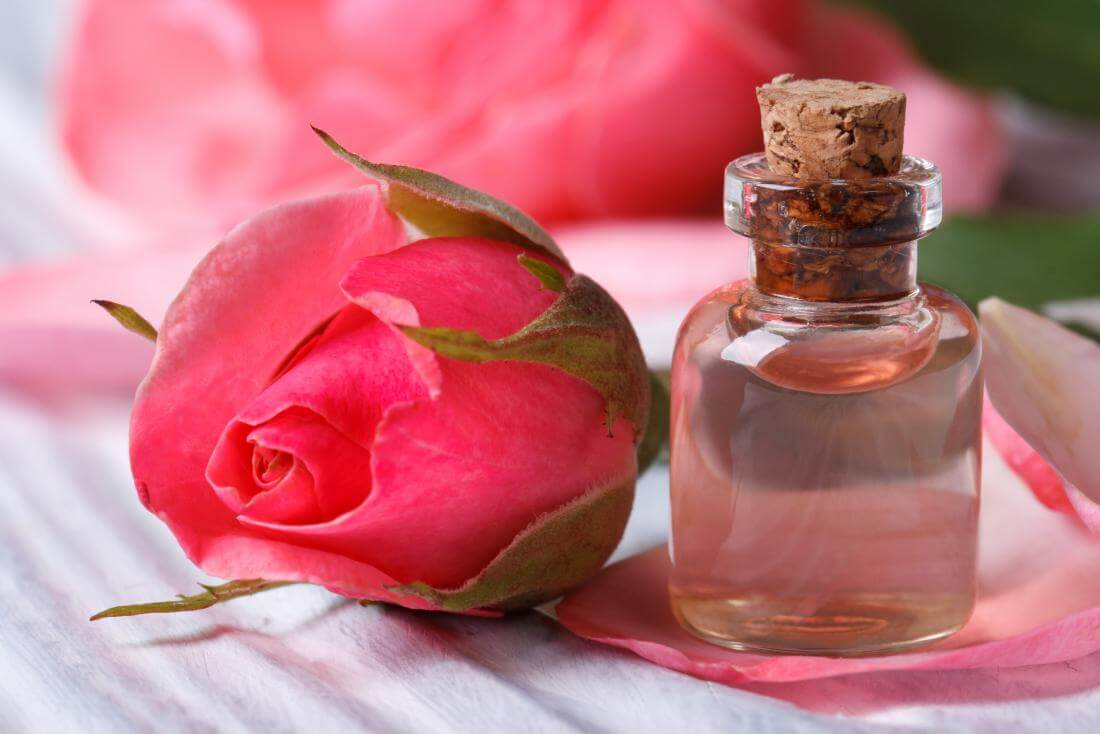 Rose water in small glass bottle next to rose flower